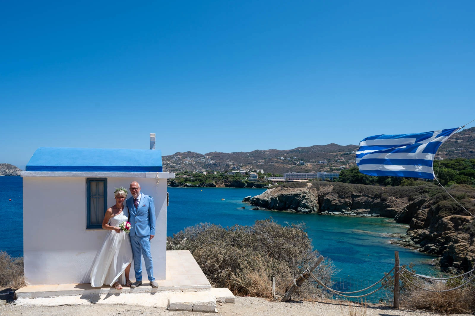Couple portrait next to traditional Greek chapel overlooking Agia Pelagia bay in Crete