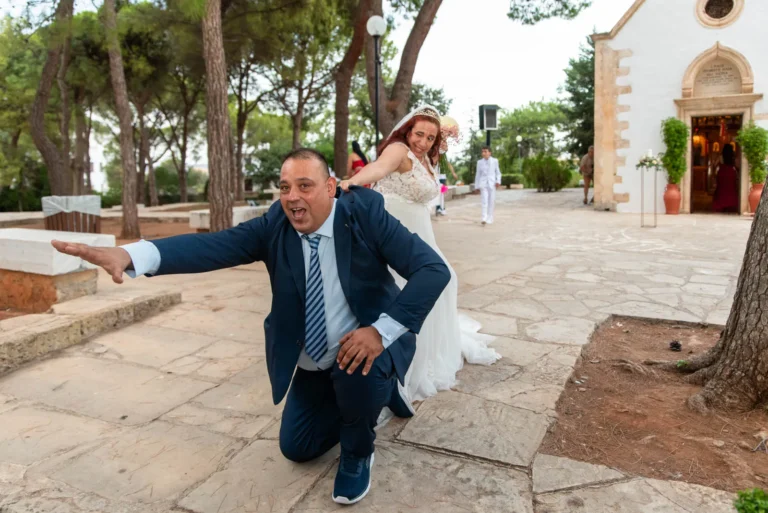 Amalia & Antonis — Orthodox Wedding at Profitis Ilias Akrotiri, Chania 1 Fun just married moment with groom kneeling and bride laughing outside Profitis Ilias church in Akrotiri Chania Crete