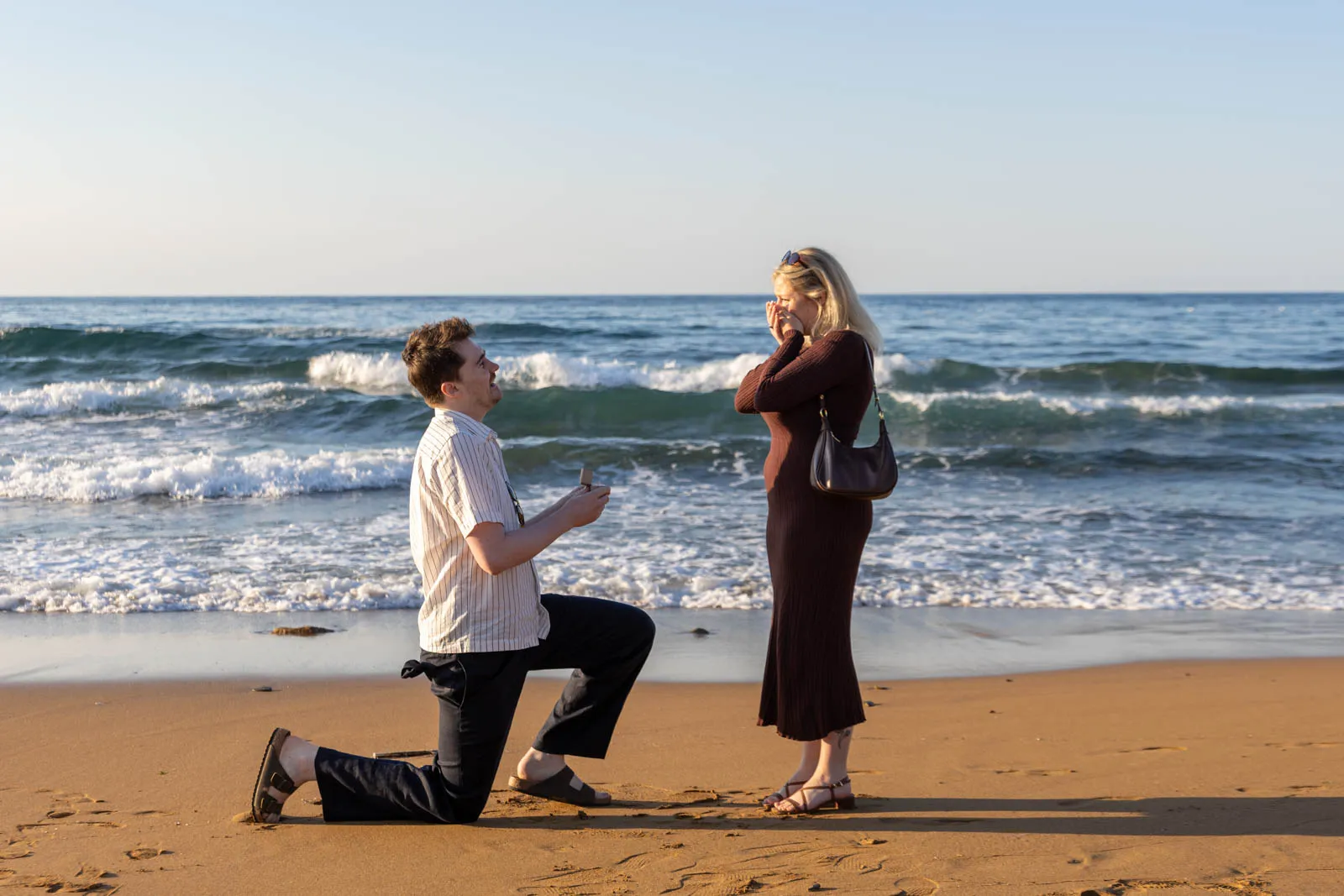 Euan preparing to propose while Imogen looks toward the sea at Stalos Beach